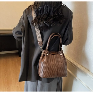 Detail of woven bucket bag with colorful wide shoulder strap and gold hardware accents