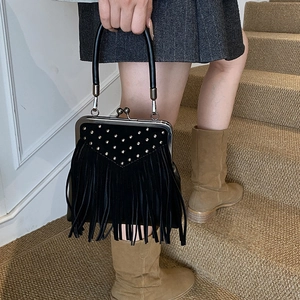 Detail of black suede handbag featuring tassel fringe and metallic rivets held by model