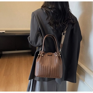 Brown woven bucket bag with patterned strap shown on shoulder in a lifestyle setting