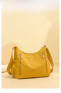 Detail of a ginger yellow oxford cloth crossbody bag with functional double front zippers