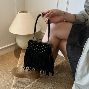 Detail of black suede handbag featuring silver rivets, tassels and a classic kiss-lock closure