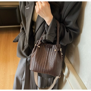 Detail of dark brown woven leather bucket bag with geometric strap and gold hardware