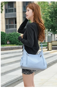 Close-up of light blue Oxford fabric crossbody bag showing multiple functional zipper pockets