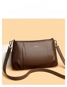 Detailed view of brown lychee texture leather crossbody bag with metal logo and wide strap