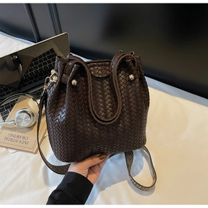 Macro view of woven dark brown leather bucket bag with gold hardware and top handle