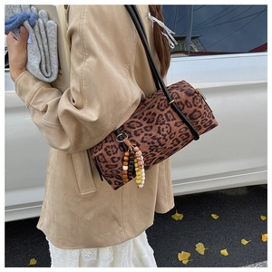 Detail of a leopard print barrel bag featuring unique beaded charms and black slim strap