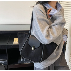 Detail of black suede tote bag featuring a polished metal lock and smooth leather trim