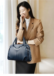 Sac à main en cuir bleu foncé avec détails argentés et deux poignées porté par un modèle