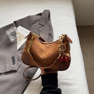 Brown suede underarm bag with gold chain and cherry charm on a grey suit jacket