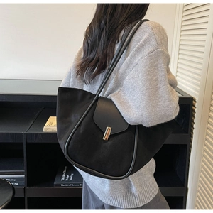 Minimalist black tote bag with gold buckle detail shown as a stylish shoulder bag on a model