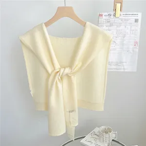 Detail of a cream knitted shawl featuring a stylish knot design on a wooden hanger