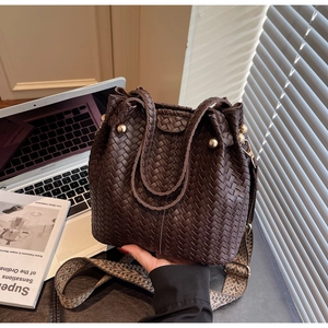 Detail of dark brown woven leather bucket bag with gold bead hardware and patterned strap