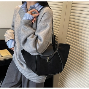 Detail of black suede tote bag with gold lock buckle and leather handle on a model shoulder
