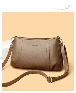 Close-up of brown litchi grain leather texture and metallic logo on the crossbody bag