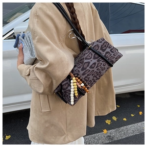 Detail of leopard print cylinder bag with colorful wooden bead tassel and black strap