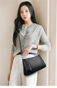 Detail of black pebbled leather crossbody bag with metallic logo on a female model
