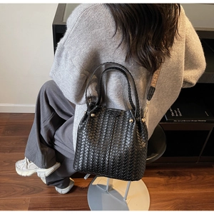 Detail of black woven bucket bag featuring metal rivets and patterned wide shoulder strap