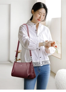 Detail view of burgundy lychee leather crossbody bag on female model with white shirt