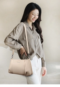 Detail of beige pebbled leather crossbody bag with metal logo and fine vertical stitching
