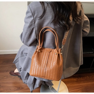Detail of a brown woven bucket bag with a geometric wide strap and metal studs