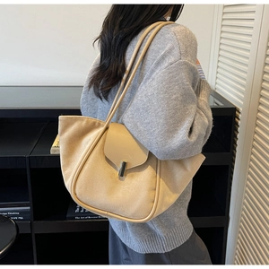 Detail of elegant beige tote bag with metallic lock closure shown on a model's shoulder