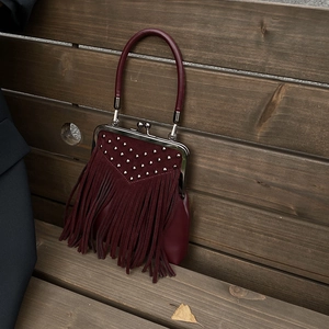 Close-up of wine red retro handbag with fringe tassels, rivets and metal frame clasp