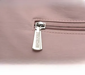 Detailed macro view of silver metallic zipper with engraved logo on pink fabric bag