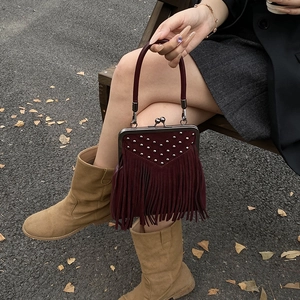 Detail of burgundy tassel handbag featuring silver studs and vintage metal frame closure