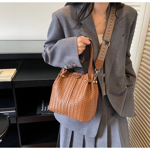 Detail of woven brown bucket bag featuring wide patterned strap and gold stud accents