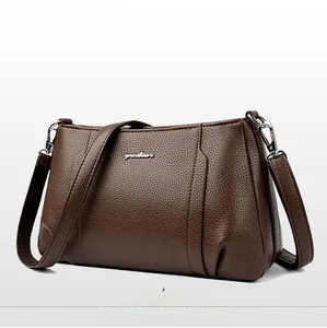 Close-up of brown litchi pattern leather texture and silver metal logo on crossbody bag