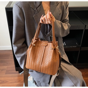 Detail of vintage woven bucket bag with jacquard strap and metallic studs on brown texture