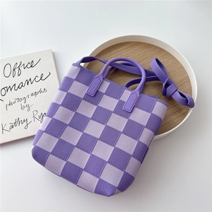 Detail of purple checkered knit bucket bag with handle and shoulder strap on tray