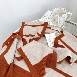 Striped knit shawl cardigan in brown and beige with a soft texture on a glass table