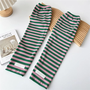 Close-up of pink and green striped knit arm sleeves with branded label on wooden surface