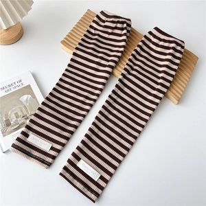 Detail of striped knitted arm warmers with brand label on a minimalist wooden tray