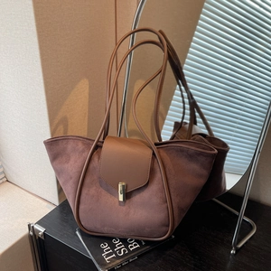 Deep brown suede bucket tote bag with leather flap and gold lock in a minimalist setting
