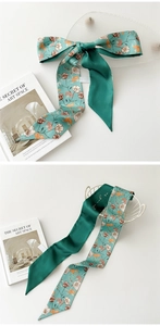 Détail d'un foulard en soie vert à fleurs noué en boucle montrant la texture satinée