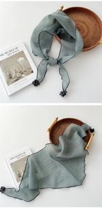 Detail of greyish-green cotton linen scarf with black pom-pom tassels and soft texture