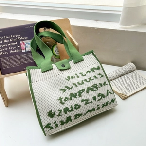 Detail of white and green knitted tote bag featuring a snap button and textured letters