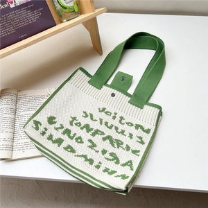 Detail of knit handbag with green lettering, snap closure and wide handles