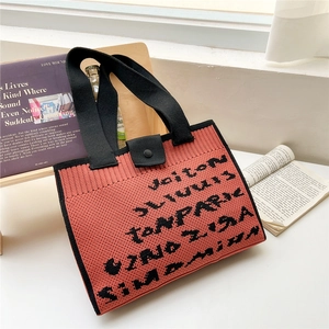 Close-up of coral pink knit tote bag texture with black handles and button closure