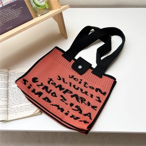 Close-up of knit tote bag with vertical stripes and black woven artistic letters