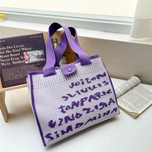 Fashionable purple and white knit tote bag with letter patterns on a white table