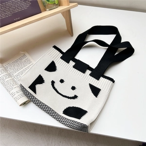 Close-up of knit tote bag featuring black smiley face pattern and cow print texture