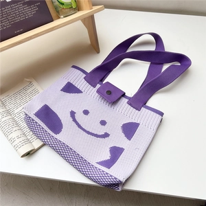 Detail of purple knitted tote bag with smiling face pattern and wide shoulder straps