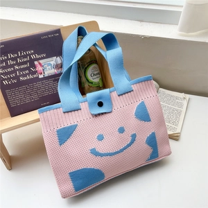 Detail of knitted tote bag with blue smiley face pattern and black button closure