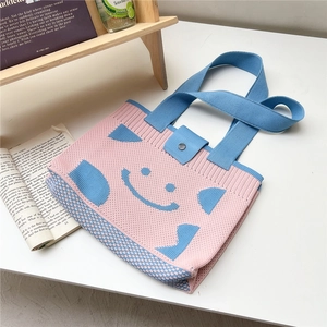 Detail of knitted tote bag showing blue smiley face pattern and metal snap button closure