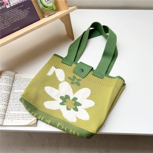Detail view of green knitted tote bag featuring a white flower and black snap button closure