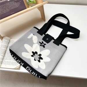 Detail of floral knit tote bag showing thick black handles and woven flower texture