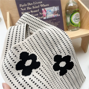 Close-up of a cream knitted tote bag with black flower patterns on a wooden shelf